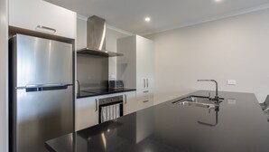 A modern kitchen with stainless steel appliances, a black countertop, and a built-in oven. - Modern work-ready Hamilton home with sauna and EV charging (Waikato)