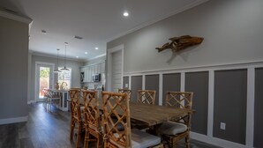 Comedor con mesa y sillas de madera, cocina al fondo y un elemento decorativo en la pared.