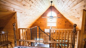 Un intérieur en bois avec un plafond en pente, un lit recouvert d’une couverture à motifs, une chaise en bois et une fenêtre avec des stores.