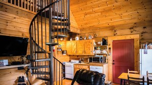L’intérieur chaleureux d’un chalet avec un escalier en colimaçon, des murs en bois, un coin repas et une cuisine dotée de meubles en bois.