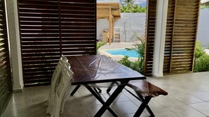 Eine Terrasse mit Tisch und Stühlen, im Hintergrund ein Pool und Holzjalousien.