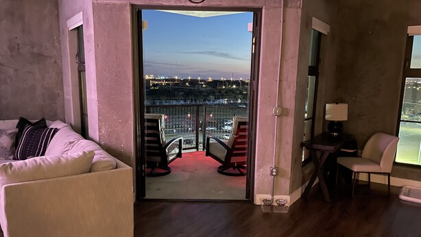 A living room with a sofa, a small table with a lamp, and a view of a cityscape through a glass door. - Prime Rental Location for Super Bowl LV Experience (Tampa)