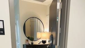 A hallway with a wooden floor, a black and white checkered doormat, a mirror, a lamp, and a cabinet. - Prime Rental Location for Super Bowl LV Experience (Tampa)