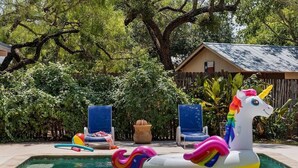 Una piscina con juguetes inflables, incluyendo un flotador con forma de unicornio, rodeada de sillas y una casa.