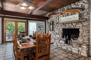 Cozy dining area with a fireplace, wooden table, and chairs, surrounded by a stone wall with a personal sign.