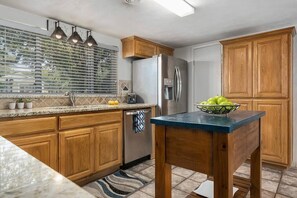 Enjoy cooking in this well-equipped kitchen with a stainless steel refrigerator, sink, and wooden table.
