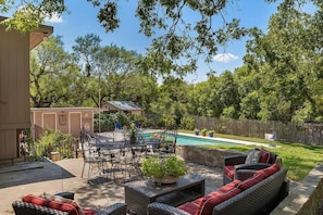 Relax by the pool in a serene outdoor space with a dining table, wicker sofa, and lush surroundings.
