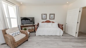 A bedroom with a bed, a TV, a wicker sofa, and a door. - Beachfront living and Big Sunsets! (Navarre)