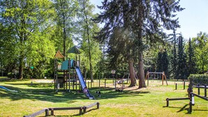 Une aire de jeux avec des toboggans et des balançoires, entourée d’arbres.