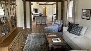 A spacious living area with a high ceiling, wooden beams, a sofa, a coffee table, and a patterned rug.