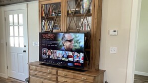 A living room with a large flat-screen TV mounted on a wooden cabinet, a wooden chair, and a wooden floor.