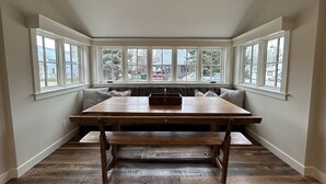 A dining area with a large wooden table, benches, and a built-in bench seating along the windows.