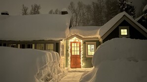 A snow-covered house with a wooden door and windows, surrounded by snowbanks.