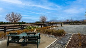 Une table de pique-nique et des bancs dans un parc, avec un chemin de gravier et une clôture en bois.