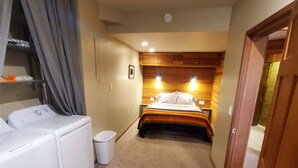A bedroom with a bed, a washing machine, and a small trash bin. - Cozy Downtown Guesthouse (Silverton)