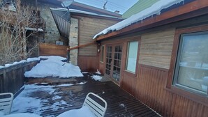 A wooden deck with snow accumulation, a satellite dish, and a wooden building with large windows. - Cozy Downtown Guesthouse (Silverton)