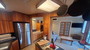 A modern kitchen with wooden cabinets, a stainless steel refrigerator, a microwave, and a stove. There is a dining area with a table and chairs, and a living room with a sofa and a TV. - Cozy Downtown Guesthouse (Silverton)