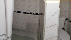 Een badkamer met witte marmeren tegels, een toilet en een douchegedeelte.