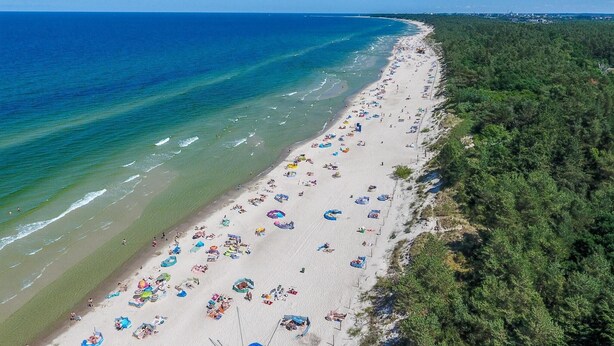 Luchtbeeld van een strand met veel parasols en mensen.