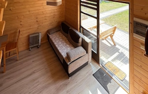 A wooden interior with a sofa, a radiator, and a view of the outside.