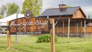 A wooden sign for Point of the Bluff Vineyard & Tasting Room with a rustic building in the background.