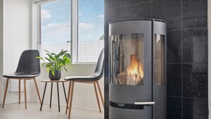 A modern living room with a glass-fronted fireplace, two chairs, a small table with a plant, and a window with blinds. - Pet friendly home in Grenaa with WiFi (Grenaa)