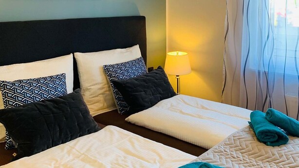 Ett hotellrum med två sängar, var och en med ett vitt överkast och svartvita mönstrade kuddar. Det finns en lampa på nattduksbordet och ett fönster med gardiner.