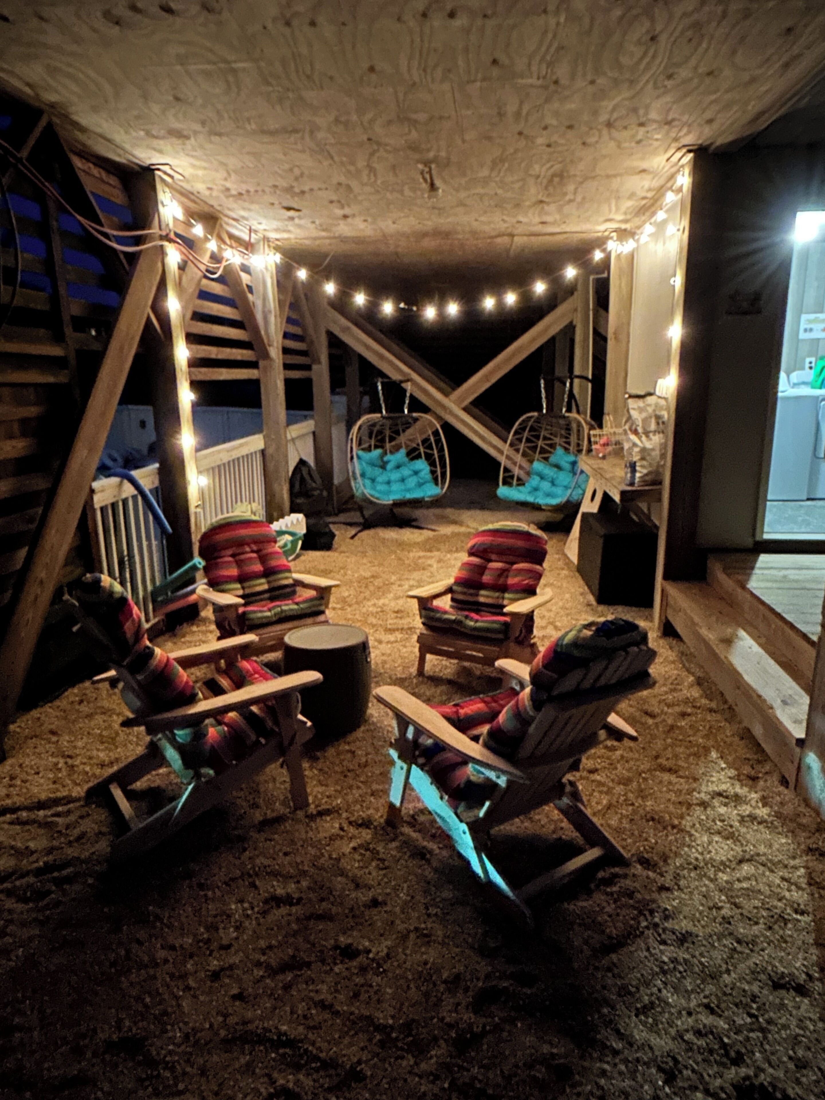 A cozy outdoor seating area with wooden chairs and a swing chair, surrounded by string lights.