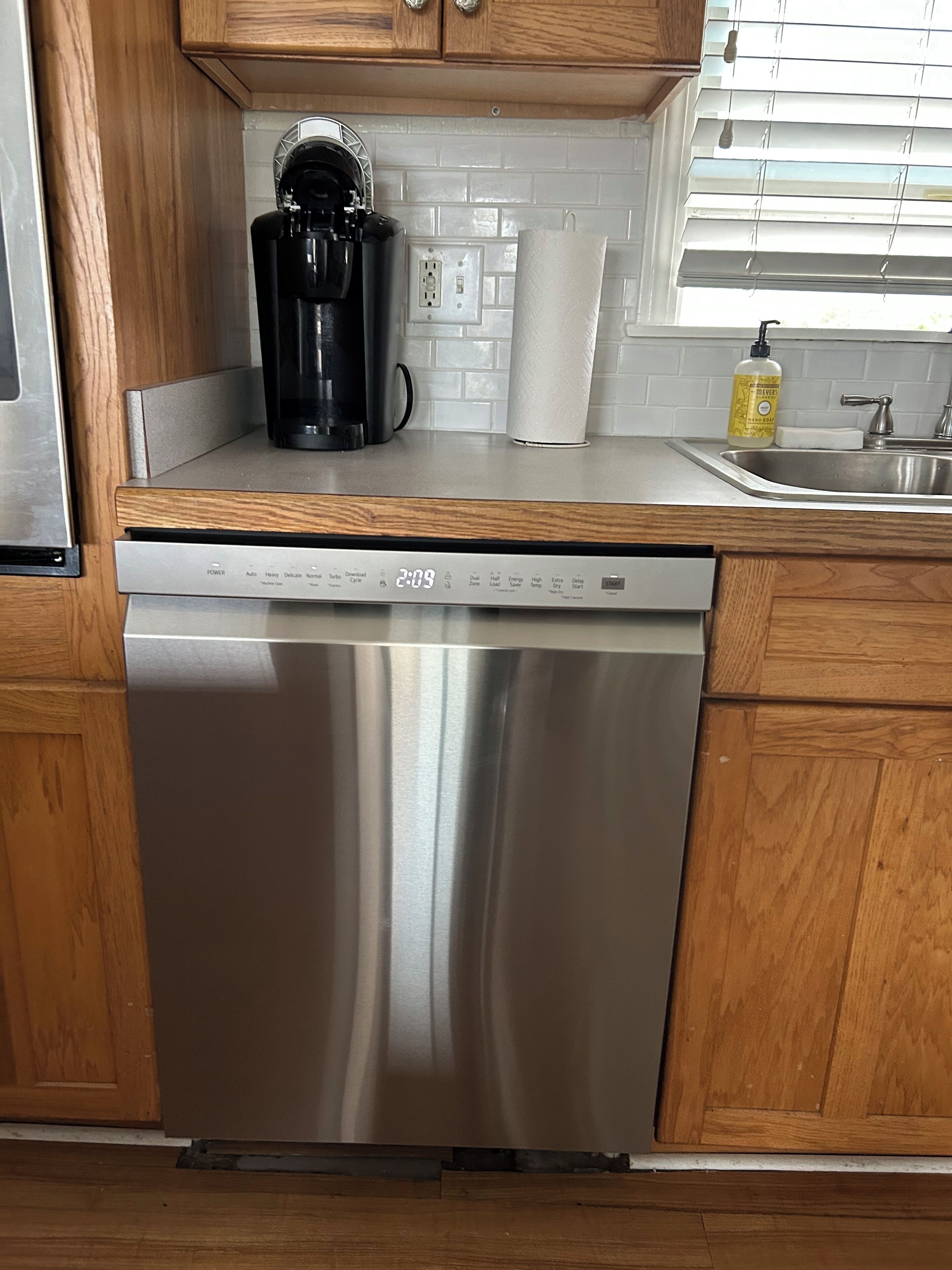 A stainless steel dishwasher in a kitchen with wooden cabinets and a white tiled backsplash.
