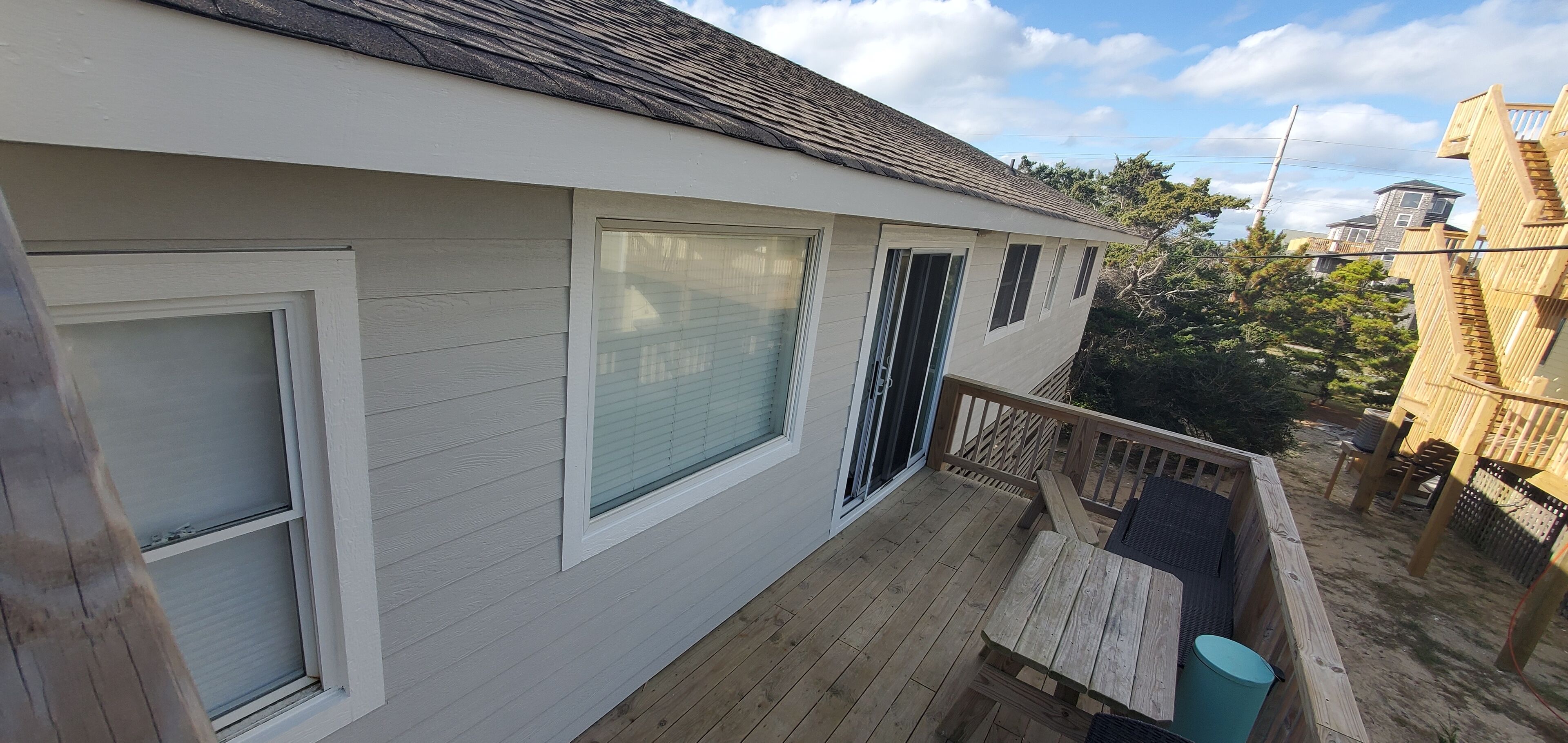Ein zweistöckiges Haus mit einer Holzterrasse, großen Fenstern und einem Balkon.
