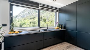 Une cuisine moderne avec des meubles de couleur sombre, une grande fenêtre donnant sur les montagnes et un panier de fruits posé sur le comptoir.