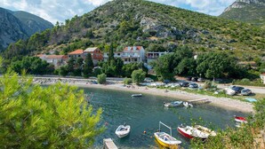 Un village côtier avec des maisons construites sur une colline, une plage animée et des bateaux amarrés au bord de l’eau.