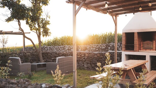 An outdoor patio with wicker furniture, a stone wall, and a brick oven.
