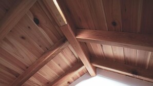 A bedroom with a wooden ceiling and a sloped roof, a wooden headboard, and a bed with white bedding.
