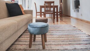 A spacious living area with a high wooden ceiling, a sofa, a dining table with chairs, and a patterned rug.