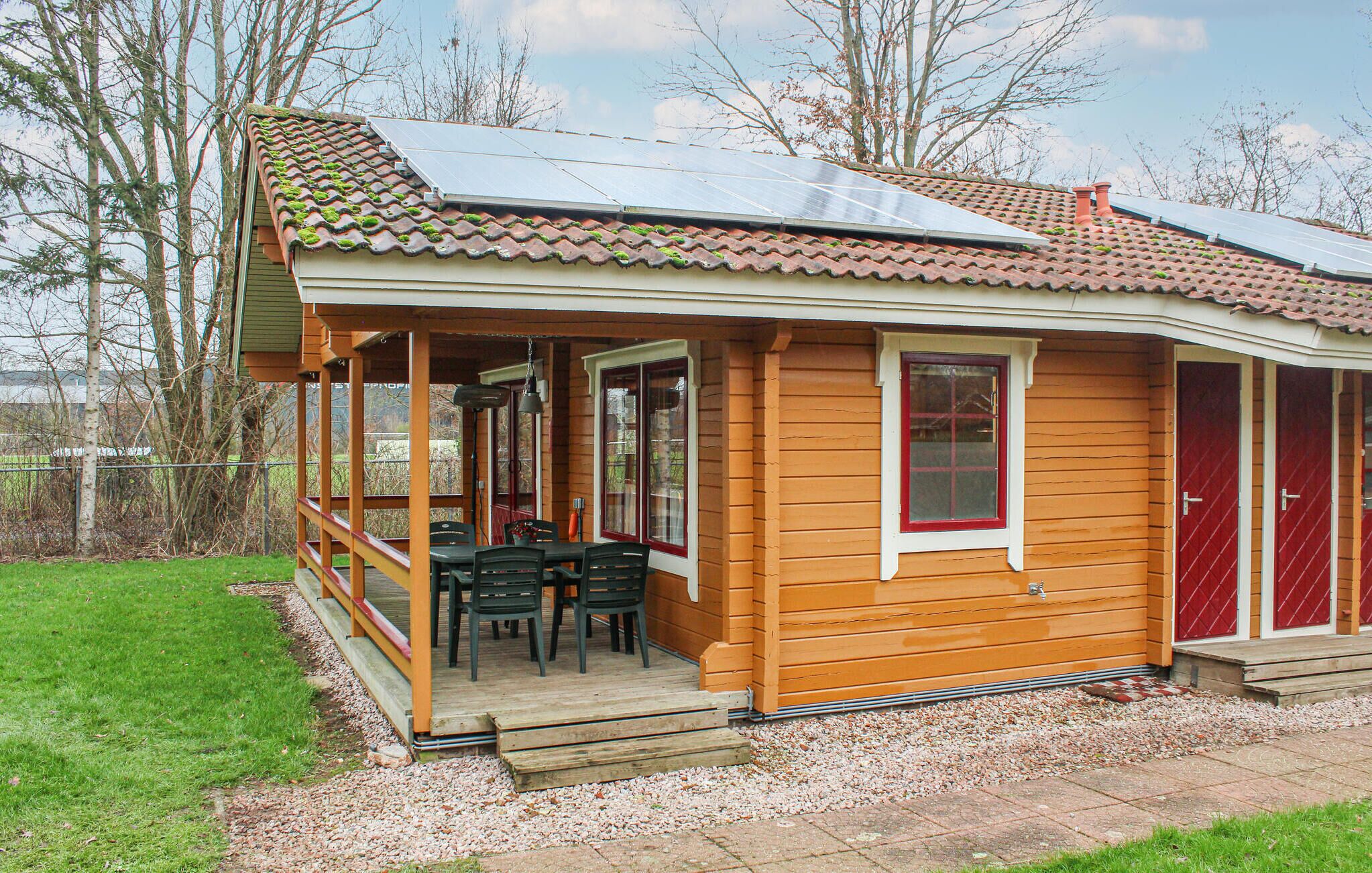 Een houten vakantiehuis met een pannendak, een veranda met stoelen en een rode deur.