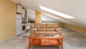 A spacious attic room with a sofa, a glass-top coffee table, a washing machine, and a skylight. - Lovely apartment in Málaga with WiFi (Málaga)