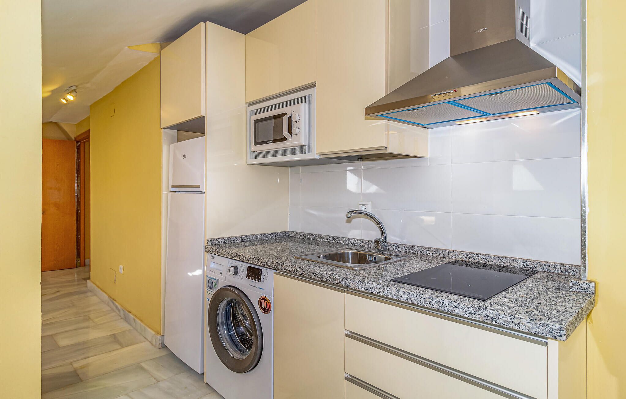 Cocina compacta con microondas integrado, lavamanos de acero inoxidable y lavadora.