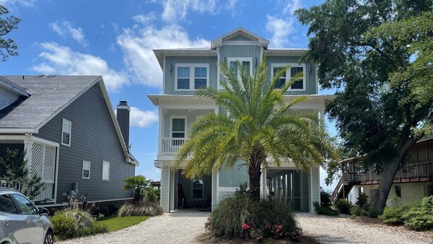 A two-story house with a gravel driveway, a palm tree, and a car parked on the left. - Charming studio with pier on Mobile bay (Fairhope)