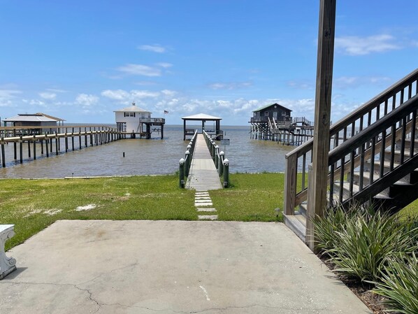 A pier leading to a wooden structure with a covered area, a small white building, and a larger wooden building with a green roof.