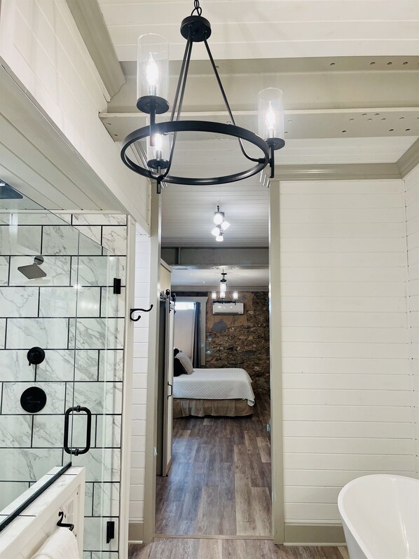 Un baño moderno con cabina de ducha de vidrio, azulejos de mármol, una bañera independiente y una araña.