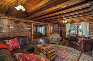 L’intérieur d’une cabane en rondins, avec un plafond en bois, un canapé en cuir, un petit fauteuil et une malle ancienne.