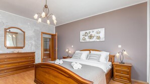 Un dormitorio con una cama de madera, mesitas de noche con lámparas, un espejo y un baño visible a través de una puerta abierta.