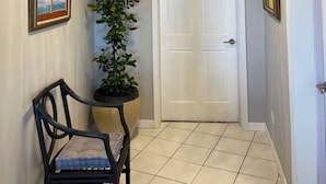Un couloir avec une porte blanche, une plante en pot, un tableau encadré et une chaise.