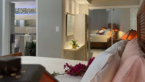 Une chambre moderne avec un lit, une table de chevet et un miroir. On peut admirer, depuis la chambre, un balcon donnant sur un paysage urbain.
