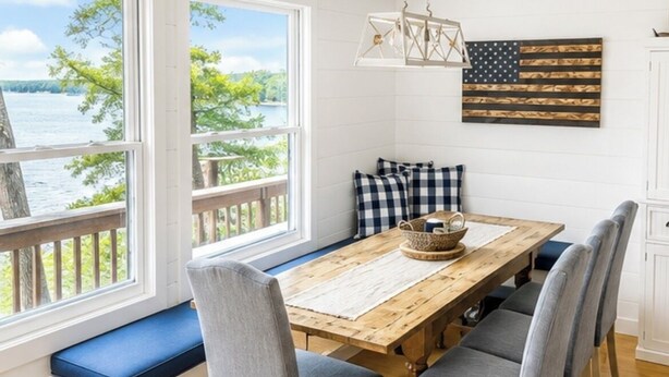 A dining area with a wooden table, grey upholstered chairs, a bench with blue cushions, and a view of the lake. - Lakefront, 3 Amazing Decks, Tennis/Pickle Ball, Boat Slip, Hot Tub, Bed Swing
 (Oakland)
