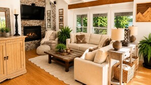 A living room with a fireplace, a sofa, a coffee table, and a TV mounted on the wall. - Lakefront, 3 Amazing Decks, Tennis/Pickle Ball, Boat Slip, Hot Tub, Bed Swing
 (Oakland)