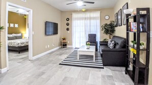 A living room with a sofa, a coffee table, a TV, and a bookshelf. - Homely spacious 2BD Close to Disney (Kissimmee)