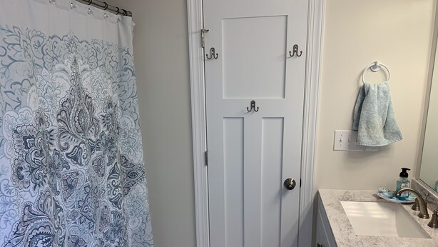 Une salle de bain avec un rideau de douche, une porte blanche, un porte-serviettes, un lavabo avec un miroir et un distributeur de savon.