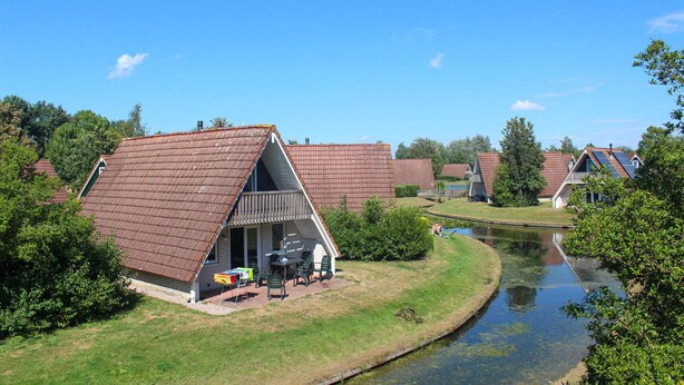 A row of traditional A-frame cottages with attached porches, a small pond, and surrounding greenery. - 3 bedroom stunning home in Gramsbergen (Gramsbergen)